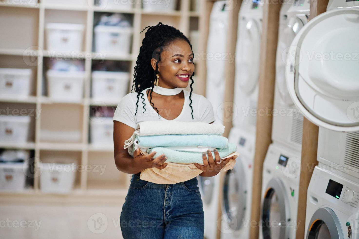cheerful-african-american-woman-with-towels-in-hands-near-washing-machine-in-the-self-service-laundry-photo
